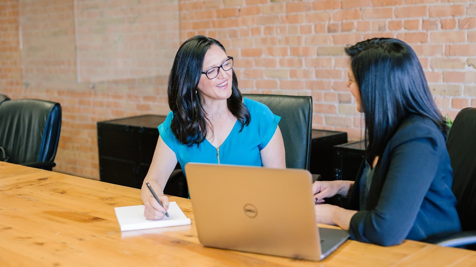Two colleagues talking over a laptop at a wooden table